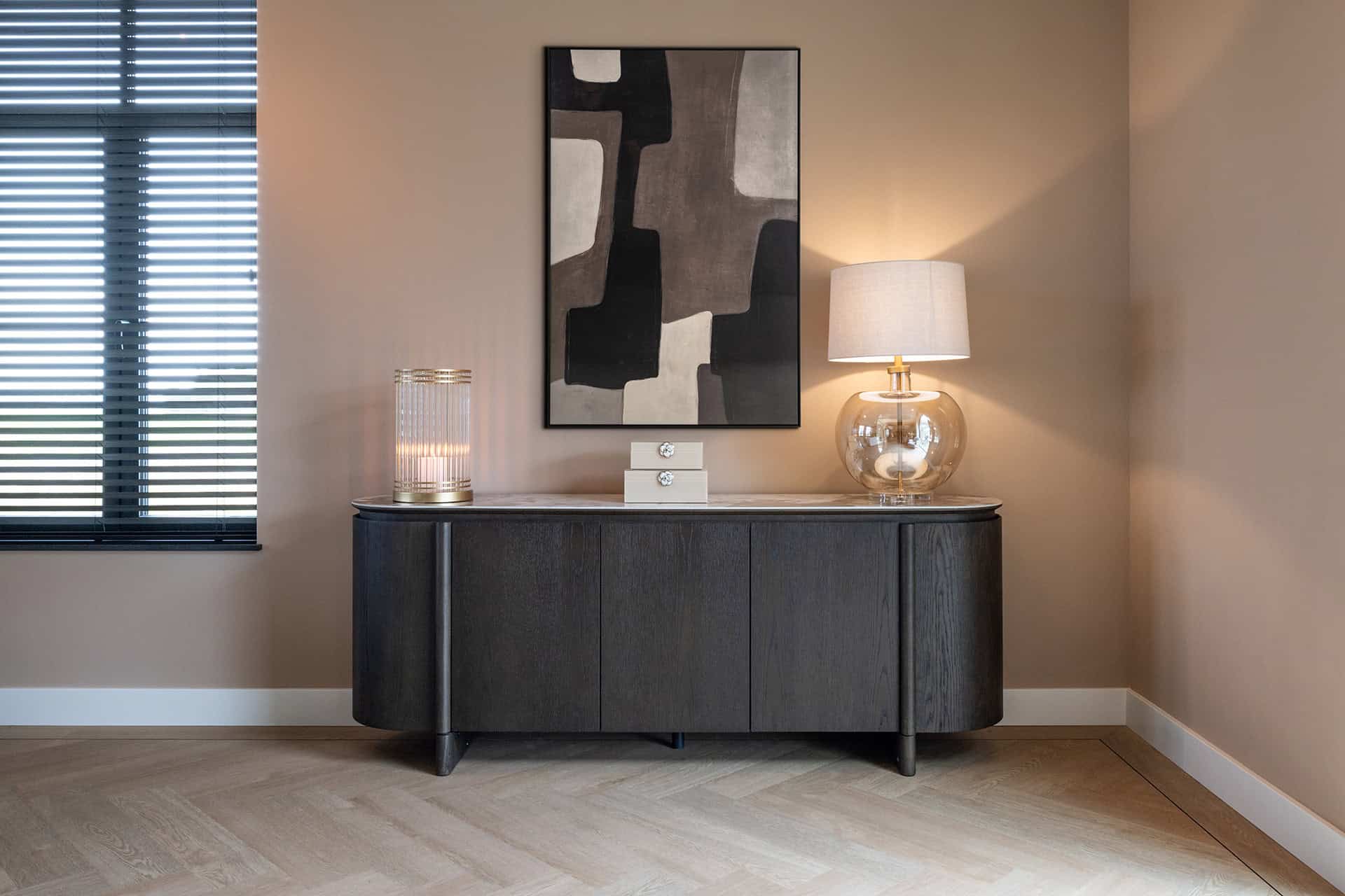 Elegante zwarte dressoir in modern interieur met abstract kunst, sfeervolle verlichting en neutrale muurkleuren.
