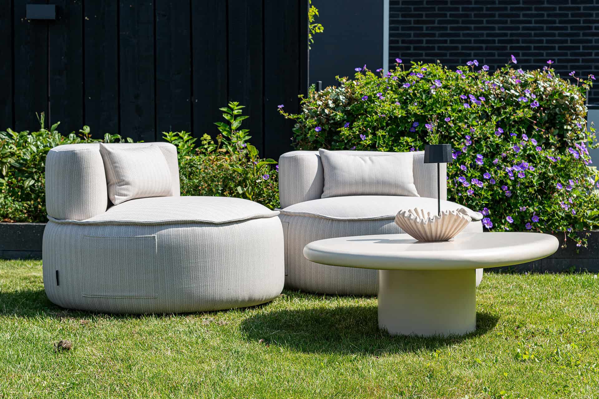 Luxury patio set with white lounge chairs and a coffee table, surrounded by a blooming garden.