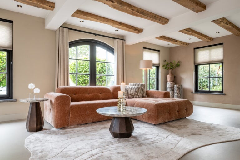 Luxe woonkamer met designbank en houten balken, subtiele verlichting en grote ramen.