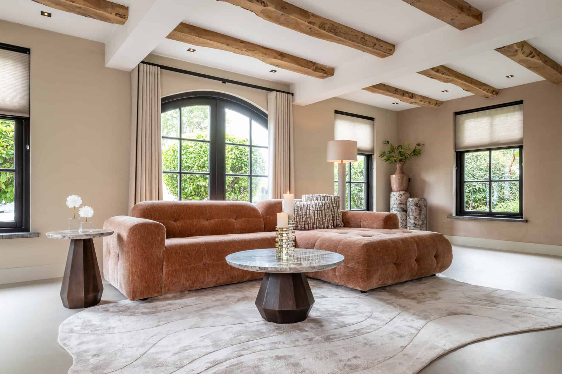 Salon luxueux avec un canapé design et des poutres apparentes, un éclairage tamisé et de grandes fenêtres.