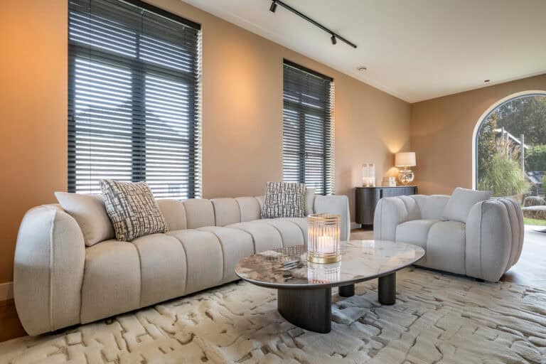 Luxe woonkamer met beige stoffering, grote ramen met jaloezieën en stijlvolle accessoires.