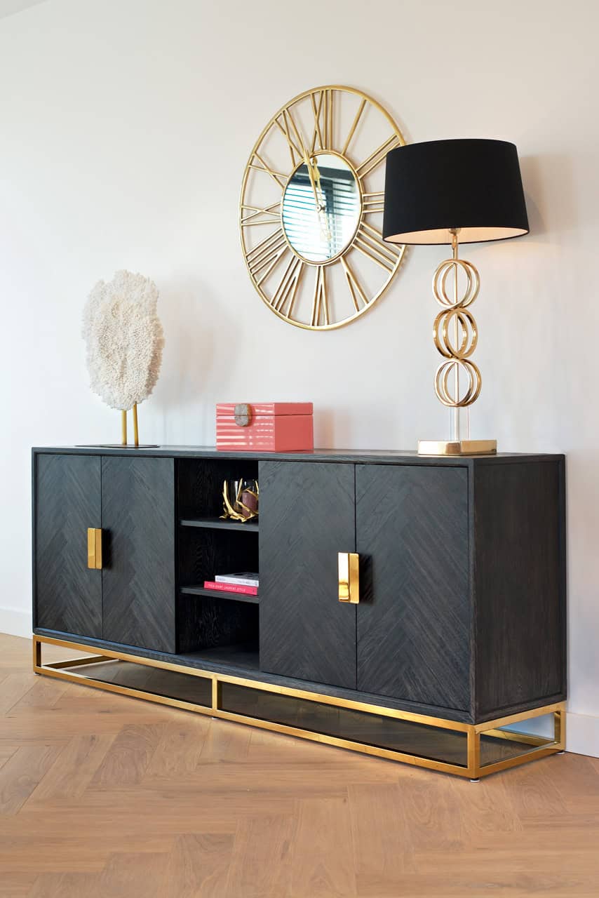 Zwart dressoir met gouden accenten, decoratieve lamp en muurklok in een modern interieur.