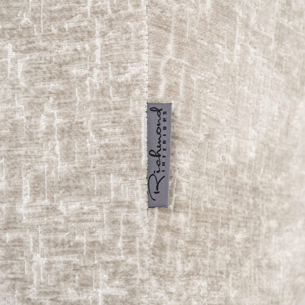 Close-up van een textielsticker met Richmond Interiors logo op een beige stoffen achtergrond.