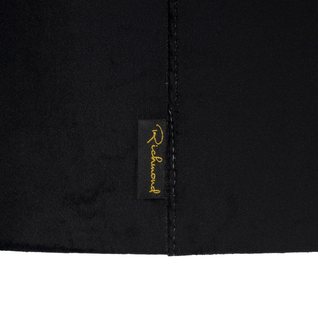 Close-up van een zwart textielproduct met Richmond logo in goud.
