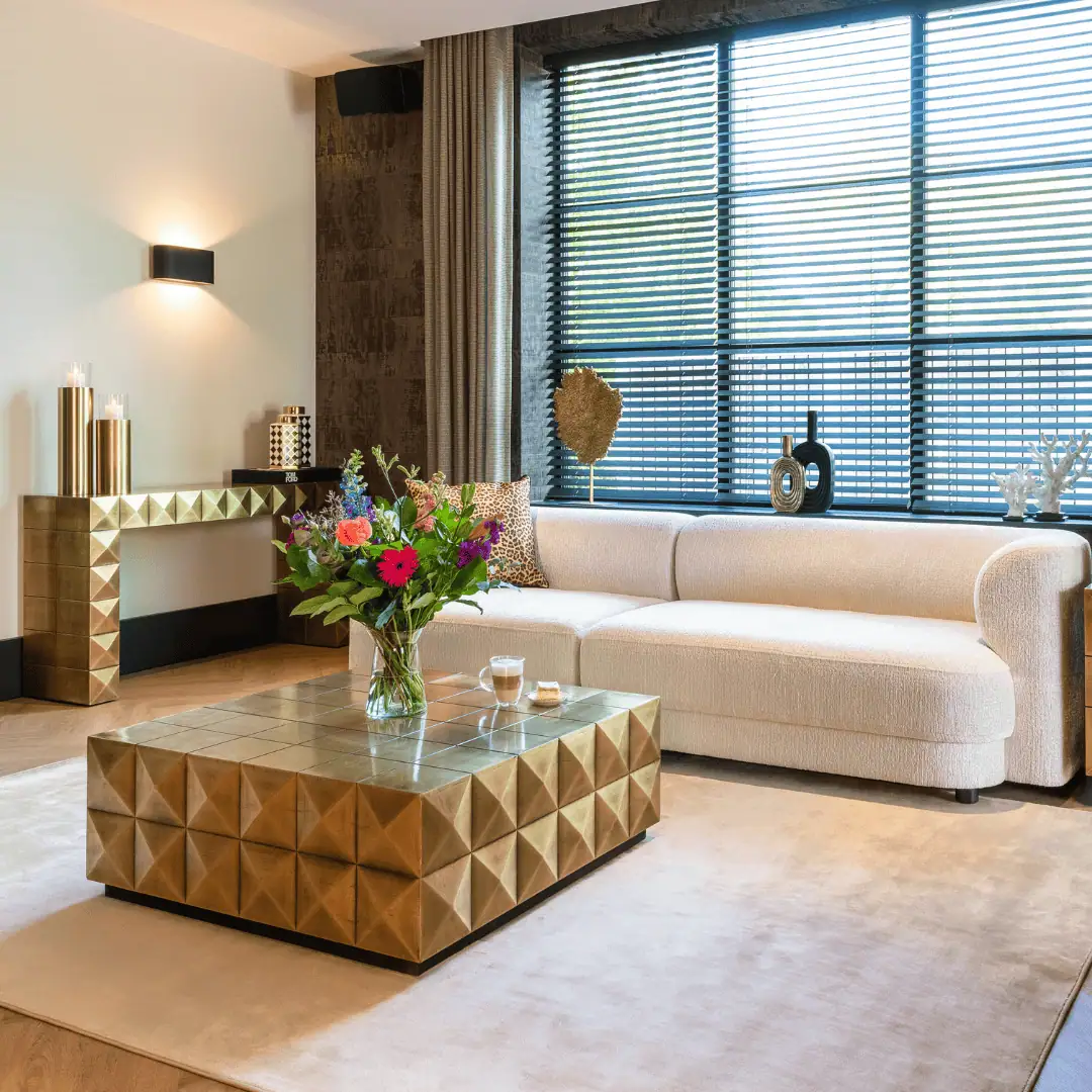 Moderne woonkamer met grote ramen, beige bank en gouden decoraties.