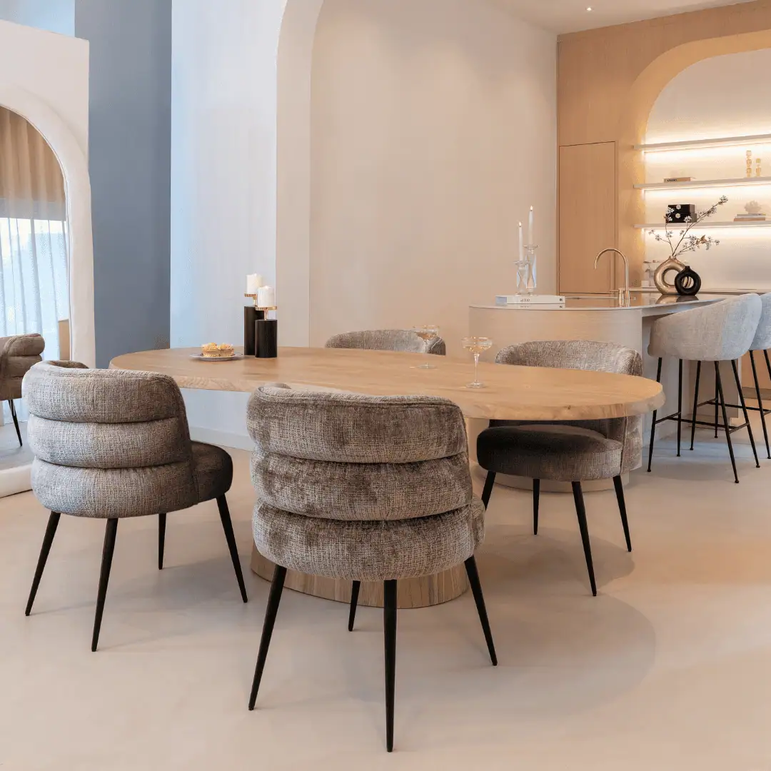 Eetkamer met houten tafel en zachte stoffen stoelen in een lichte ruimte.