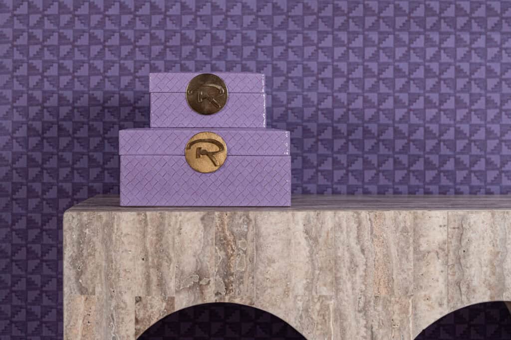 Boîte de rangement violette « Joelle » ornée d'un logo «R» doré, posée sur une table en marbre.